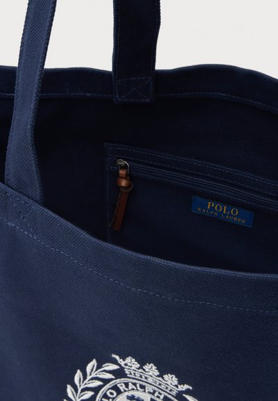 Navy blue Polo Ralph Lauren tote bag with visible interior zip pocket and leather zipper pull, showing part of the white embroidered logo.