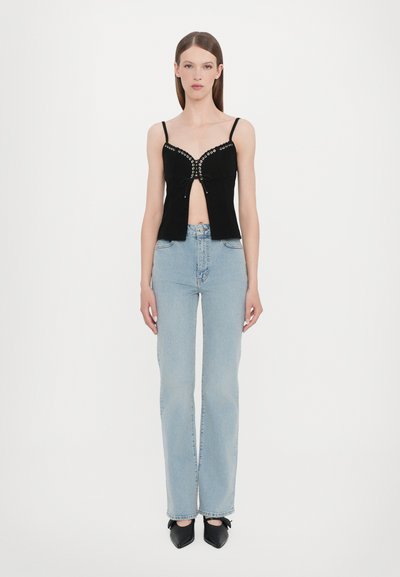 Black sleeveless top with eyelet detail and a front tie, paired with light blue straight-leg jeans and black pointed-toe shoes.