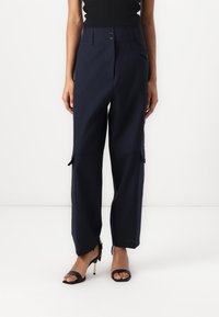 Pantalon marine avec une coupe ajustée, doté de deux boutons à la taille, de poches cargo sur les côtés et d'un tissu lisse et texturé.