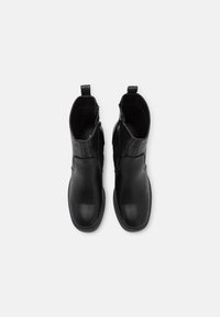 Paire de bottines en cuir noir avec fermetures éclair latérales et languettes, vues de dessus sur un fond blanc.