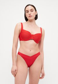 Punainen bikinit-setti, jossa on rakenteellinen, tukevalla langalla varustettu yläosa leveillä olkaimilla sekä yhteensopiva matalavyötäröinen alaosa V-muotoisella suunnittelulla. Sujuva pinta.