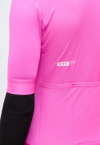 Κοντινή λήψη ενός ροζ ποδηλατικού τζέρσεϊ με μαύρα μανίκια, που φέρει το λογότυπο "SRK Sportful Riders Kit" και μια πίσω τσέπη.