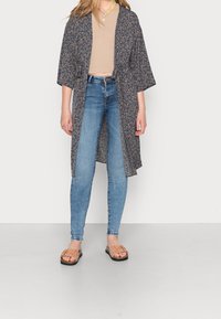 Floral-print Kimono in Dunkelblau, leichtes Material, lockerer Schnitt, offene Vorderseite. Kombiniert mit hellblauen Skinny-Jeans und beigen Rutsch-Sandalen.