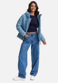 Helles blaues Pufferjacke mit Kapuze, gestepptem Design, kombiniert mit hochgeschnittenen, lässigen blauen Jeans und weißen Sneakers.