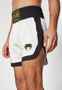 Mustvalged musta ja valgega sportlikud lühikesed püksid elastse vöökohtaga, külgedel kuldne logo ja madu disain. Sile kangas külgservadega.