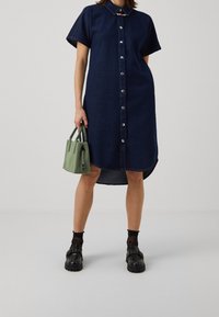 Jeansklänning med kort ärm, knappfront och krage. I kombination med en liten grön handväska och tjocka svarta skor.