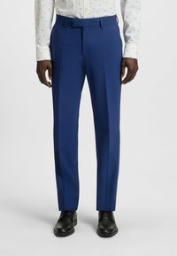 Navyblauwe op maat gemaakte broeken van gladde stof, met een rechte voorkant, riemlussen en persvouwen, gecombineerd met zwarte nette schoenen.