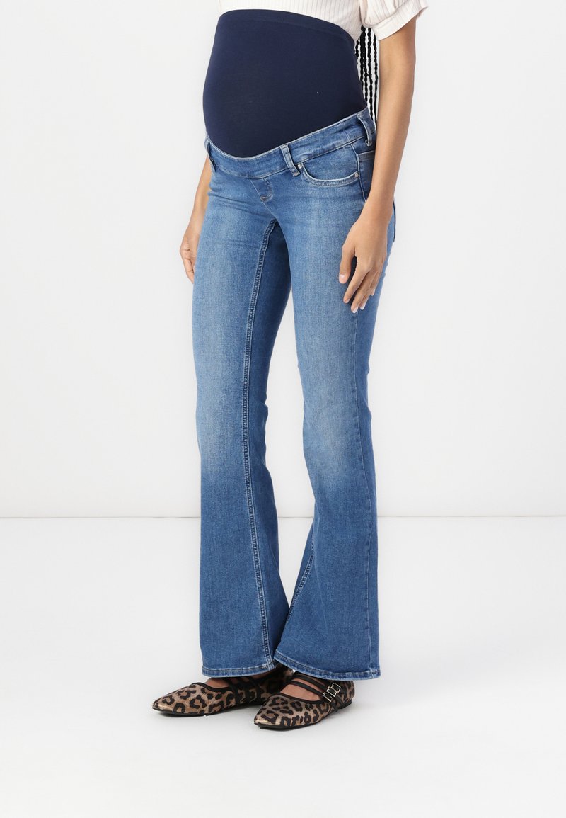 Mammabukser med bred bunn i middels blå denim med en myk marineblå stretchmidje, som har frontlommer og en lett falming på bena.
