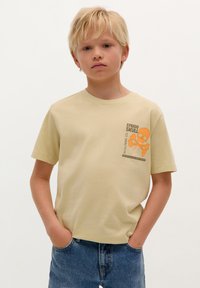 Lichtgele t-shirt met een ronde hals en korte mouwen, voorzien van een oranje schedelafbeelding en tekst op de linker borstzijde, gemaakt van katoen.