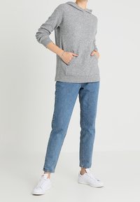 Sweat à capuche gris clair avec une poche kangourou, doté d'un cordon de serrage et de poignets côtelés, associé à un jean bleu fuselé et des baskets blanches.