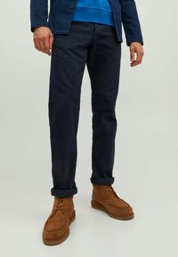 Tamno plave slim-fit hlače od pamuka u kombinaciji s tamnosmešnim ankel čizmama. Hlače imaju podvrnute manžetne i dizajnirane su za ležeran izgled.