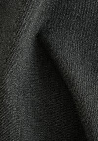 Gros plan d'un tissu noir à texture fine tissée avec des plis subtils créant des ombres douces.