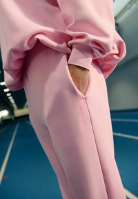 Roosa sportlik dressipluus ja püksid pehme tekstuuriga, millel on küljetasku ja minimaalne bränding ääre lähedal. Sile, keha järgnev disain.