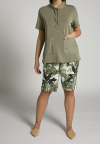 Maglietta a maniche corte verde oliva con cappuccio e due tasche frontali abbinata a pantaloni corti bianchi con un motivo a foglia tropicale verde.