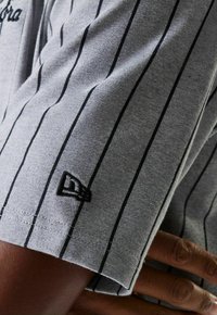 Chemise grise à manches courtes avec des rayures verticales noires, texture lisse et un petit logo brodé sur la manche.