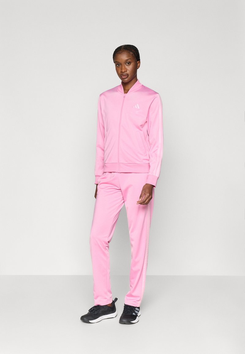 Ροζ φόρμα από απαλό, ελαφρύ ύφασμα, με μπουφάν με φερμουάρ και ριμπ μανσέτες και αντίστοιχο παντελόνι με πλευρικές ρίγες.