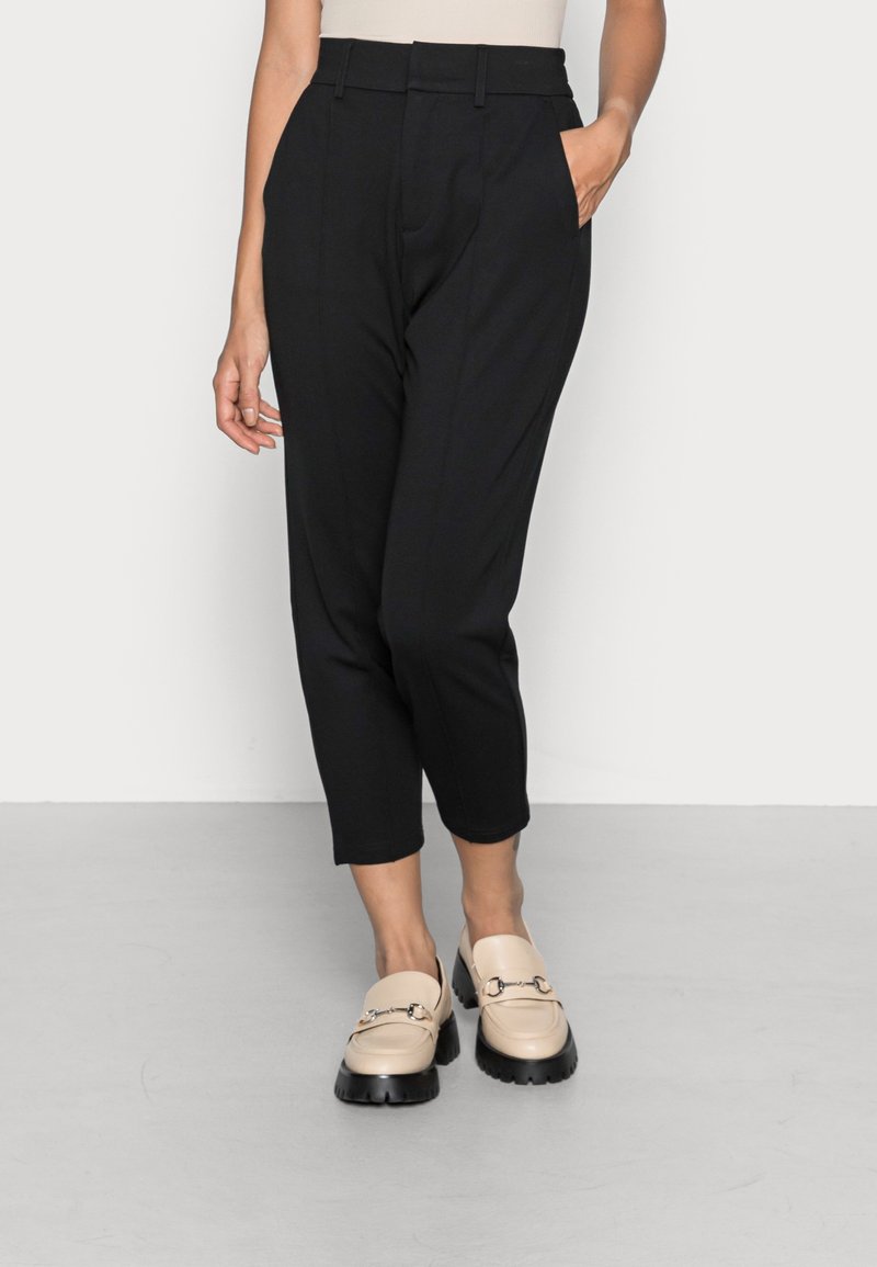 Svarta skräddarsydda byxor med hög midja, med framfickor och sidofickor. Kombinerade med beige loafers med en kraftig svart sula.