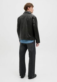Sort læderjakke med flad krave, afslappet pasform, detaljerede sømme og en glat tekstur, båret over en lys denimskjorte og mørke jeans.