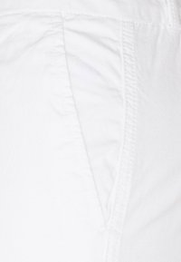 Pantaloni bianchi in tessuto con una texture liscia, caratterizzati da dettagli di cucitura discreti e un design a vita bassa. Cucitura centrale visibile.