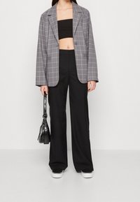 Harmaa ruudullinen bleiseri, jossa on lovetut kaulukset, yhdistetty mustaan crop topiin ja mustiin leveälahkeisiin housuihin. Asusteet sisältävät pienen mustan käsilaukun.