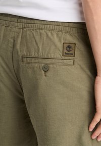 Olivové kraťasy se strukturální úpravou, s zadní kapsou uzavíratelnou knoflíkem a nášivkou Timberland nad kapsou.