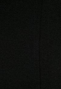 Fekete kötött szövet finom bordás textúrával és minimális varrásokkal. Rugalmas anyag a kényelem és a szoros illeszkedés érdekében.