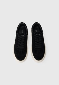 Mustad alfahallistest ketsid mustade paelte ja logo detailiga keelega. Valge kummist tald ümarate kujunditega. Sile tekstuur.