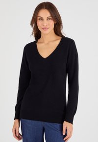 Zwarte V-hals trui van zachte stof, met lange mouwen en een licht getailleerd silhouet, in combinatie met donkerblauwe broek.