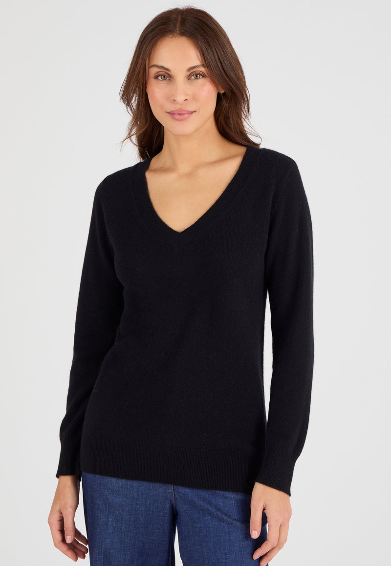 Zwarte V-hals trui van zachte stof, met lange mouwen en een licht getailleerd silhouet, in combinatie met donkerblauwe broek.