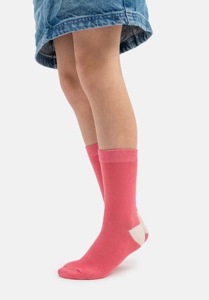Child wearing mid-calf pink socks with white heels and toes, standing on tiptoes, visible from knee to foot, wearing a denim skirt.