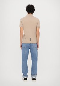 Beige polo skjorte med korte ermer, som har en teksturert stripe detalj på baksiden. Kombinert med lyseblå jeans og sko med sorte detaljer.
