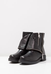 Czarne skórzane botki za kostkę z designem złożonym, z metalowymi suwakami po obu stronach i teksturowaną czarną gumową podeszwą.