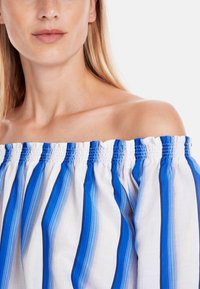 Off-the-shoulder top featuring blue and white vertical stripes, with elastic smocking detail at the neckline and lightweight fabric.