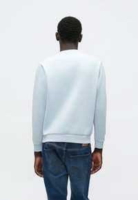 Lichtblauwe sweatshirt met een ronde hals, geribde manchetten en zoom, gemaakt van zacht stof, gezien van de achterkant met blauwe spijkerbroek.