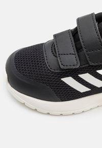 Baskets en maille noires avec semelle blanche et deux bandes Velcro noires, présentant des rayures blanches sur le côté.