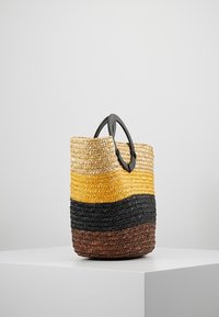 Woven straw basket with black handle, featuring a gradient of natural, yellow, black, and brown colors. Round shape and textured surface.