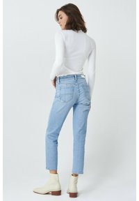 Jeans de mezclilla azul claro con corte recto, cintura alta y dos bolsillos traseros. Combinados con botas beige hasta el tobillo y una camiseta blanca de manga larga.