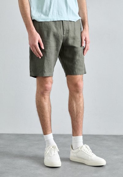Bermuda in lino verde oliva con taglio dritto, tasche frontali e texture liscia, abbinate a sneakers bianche e calzini alla caviglia.