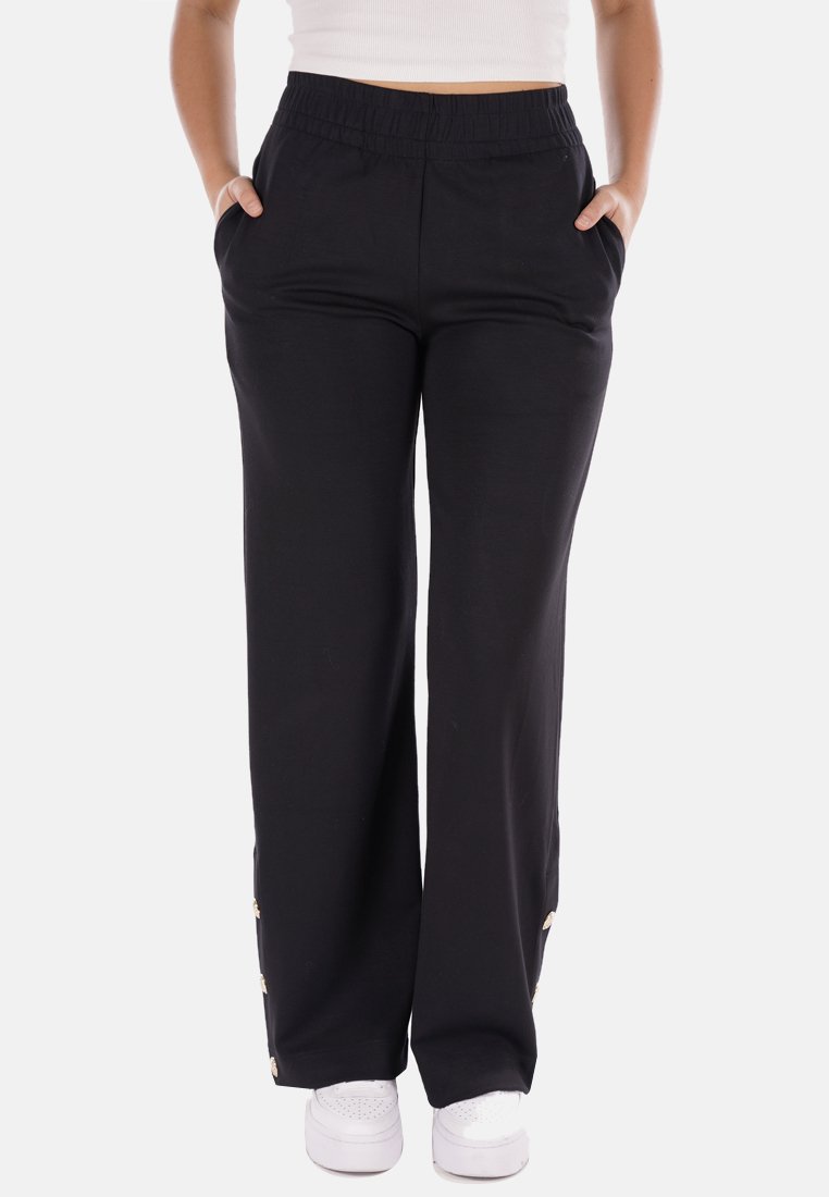 Pantaloni neri a gamba larga con cintura elastica, tasche laterali e dettagli dorati sull'orlo. Realizzati in tessuto morbido e liscio.