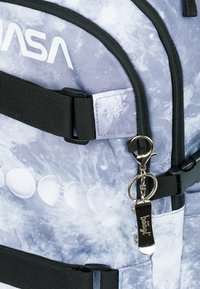 Zaino con un design grigio a tema spaziale, dotato del logo NASA, spallacci neri, cerniere e un portachiavi argentato attaccato.