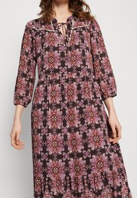 Robe longue et sombre avec des motifs floraux violets, manches mi-longues, col arrondi avec liens, et ourlet à volants. Texture de tissu lisse.