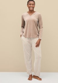 Top de terciopelo beige de manga larga con escote en V, combinado con pantalones a rayas en tonos crema y marrón claro. Textura suave, ajuste relajado.