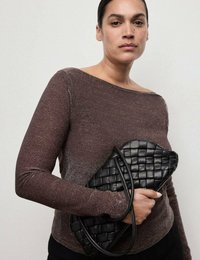 Czarna pleciona torebka trzymana w jednej ręce, z gładką skórzaną fakturą i zakrzywionym kształtem. Modelka ma na sobie błyszczący brązowy top z długim rękawem.