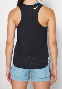 Canottiera sportiva nera con design perforato, dettagli blu sul colletto e tessuto traspirante. Abbinata a pantaloni corti azzurri.