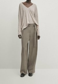Top beige à manches longues en V associé à un pantalon large taille haute de couleur marron clair. L'ensemble présente une texture subtile et une coupe décontractée.