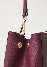 Maroon textured handbag featuring a gold-tone clip, zipper, and brass hardware accents along the edge, with a smooth black trim.