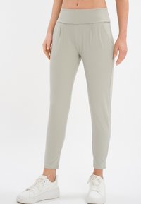 Pantaloni sportivi elasticizzati di colore grigio chiaro, con vita alta, gambe affusolate e dettagli plissettati, abbinati a sneaker bianche.