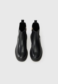 Botas negras de tobillo hechas de cuero suave, con punta redondeada, diseño sin cordones y detalles de cremallera dorada en el lateral.