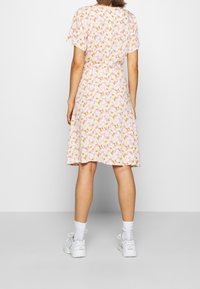 Robe à fleurs avec un fond rose, manches courtes, jupe mi-longue et taille cintrée. Portée avec des baskets blanches et des chaussettes.