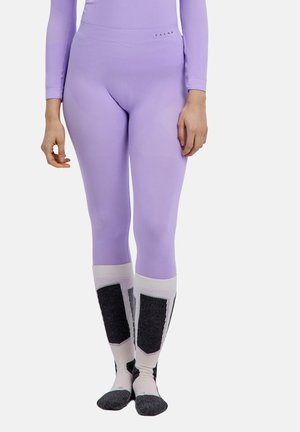 Persoon die nauwsluitende lavendelkleurige legging en lange sokken met zwart-witte geometrische patronen draagt, staand tegen een effen achtergrond.